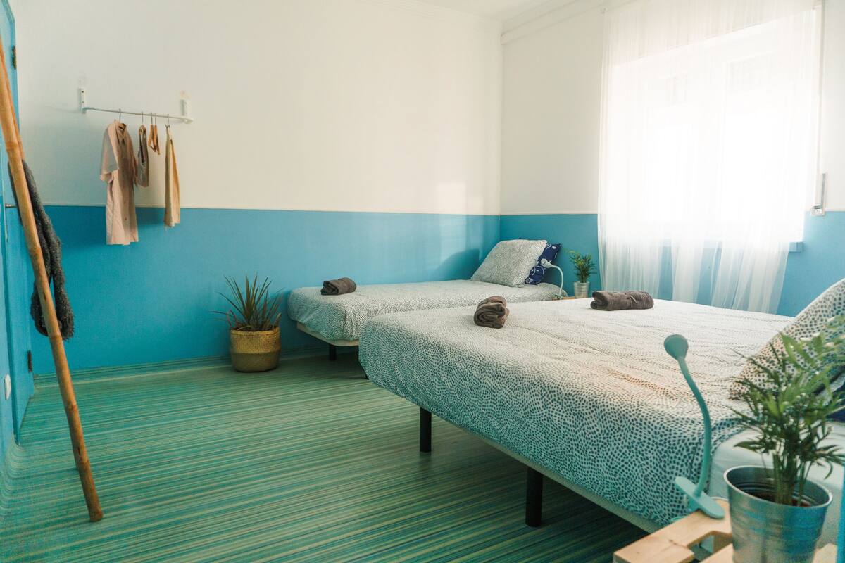 Een kamer met twee bedden, een bamboemat, een potplant en een ophangrek met handdoeken.