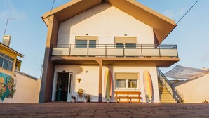 A two-story building with a balcony, a staircase, and surfboards leaning against the wall.