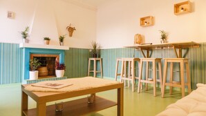 A cozy room with a wooden table, a sofa, and a fireplace. There are several stools and potted plants around.