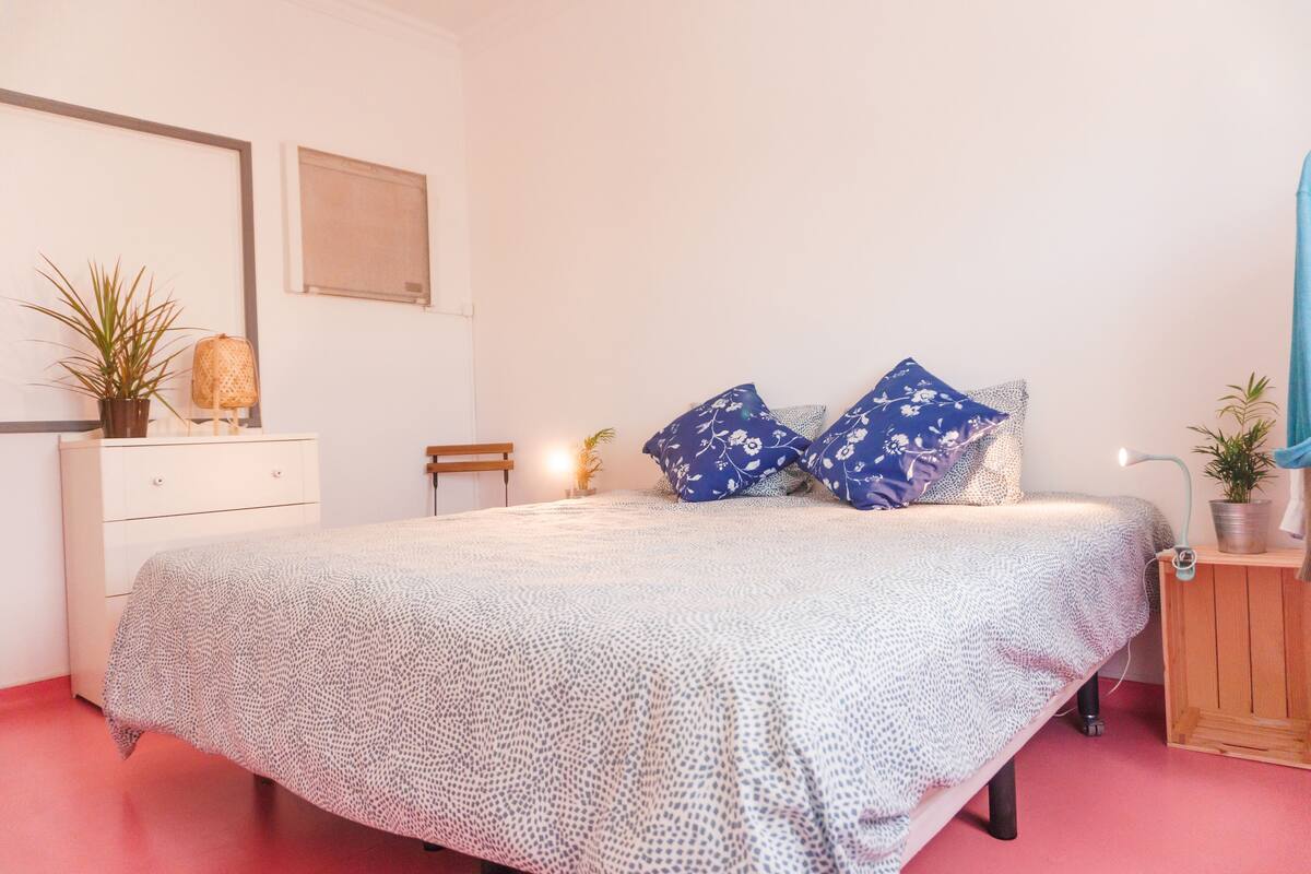 Een slaapkamer met een bed, nachtkastje, dressoir en een potplant.