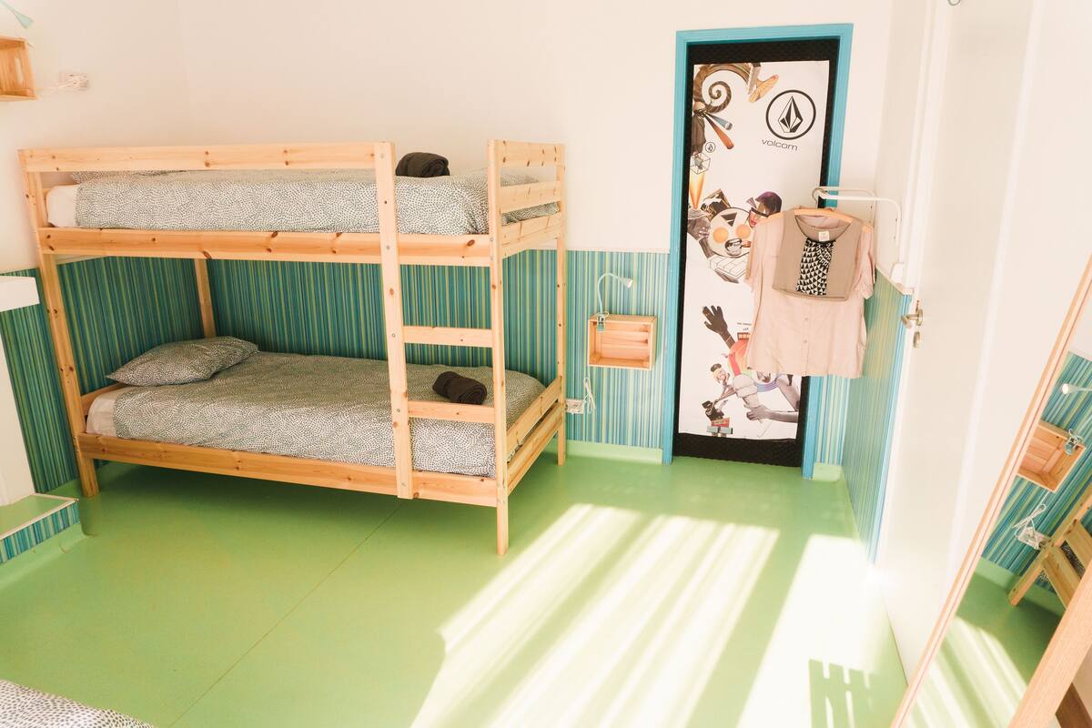 Een slaapkamer met stapelbedden, behang met strepen, een deur met een stripfiguur en een klein plankje met kleding.