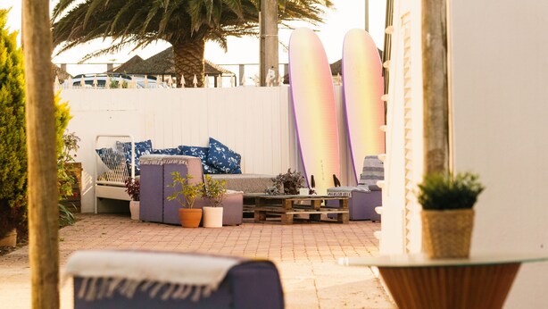 A patio area with a seating arrangement, surfboards, and potted plants.