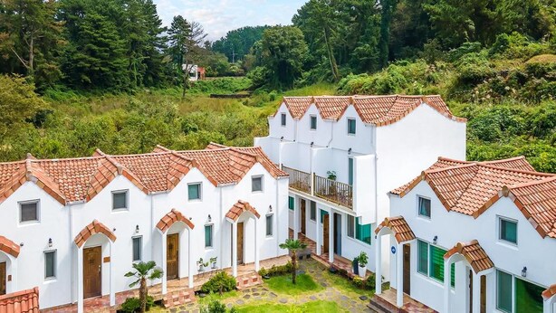 A courtyard with white buildings and red-tiled roofs, surrounded by greenery. - Jeju Eltzutown Pension (Jeju City)