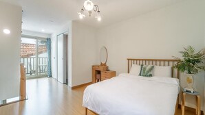 A bedroom with a large bed, a wooden nightstand, a bedside table, a mirror, and a potted plant. - Jeju Eltzutown Pension (Jeju City)