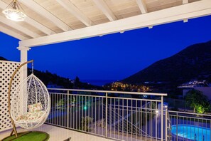 Un balcon agrémenté d’un fauteuil suspendu, une piscine et une vue sur un paysage montagneux.