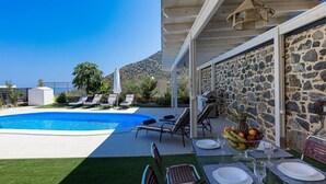 Un espace aménagé au bord de la piscine, avec un mur en pierre, des chaises longues et une table dressée pour les repas.