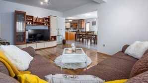 A modern living room with a flat-screen TV, a glass coffee table, and a sofa. There is a kitchen in the background with wooden cabinets and a dining area. - Vacation home with pool - a paradise for families (Žminj)