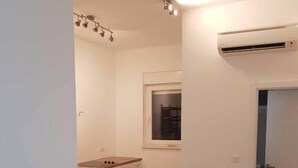 Una cocina compacta con armarios blancos, una ventana y un equipo de aire acondicionado.