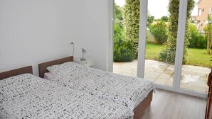 Ein Schlafzimmer mit zwei Betten, einem Nachttisch und einer großen Schiebeglasdoor zum Garten.