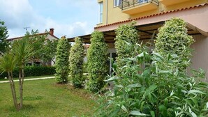 Ein Wohngebäude mit überdachter Terrasse, umgeben von gepflegter Bepflanzung und einem Rasen.
