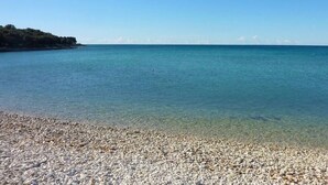 Platja de petits còdols amb aigua cristal·lina i una riba llunyana.