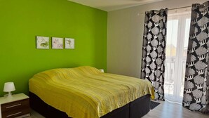 Un dormitori amb un llit, una tauleta de nit, una làmpada, una paret verda i una finestra amb cortines estampades.