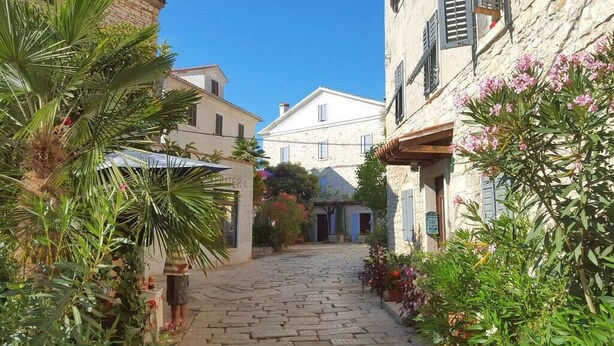 Un carrer empedrat en una localitat històrica, amb edificis de pedra, un café i vegetació abundant.