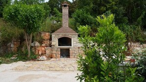Una xemeneia de pedra a l'aire lliure, construïda amb pedra, envoltada de vegetació i un camí de pedra.