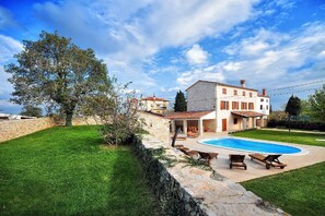 Une villa avec piscine, un mur en pierre et une pelouse verdoyante.