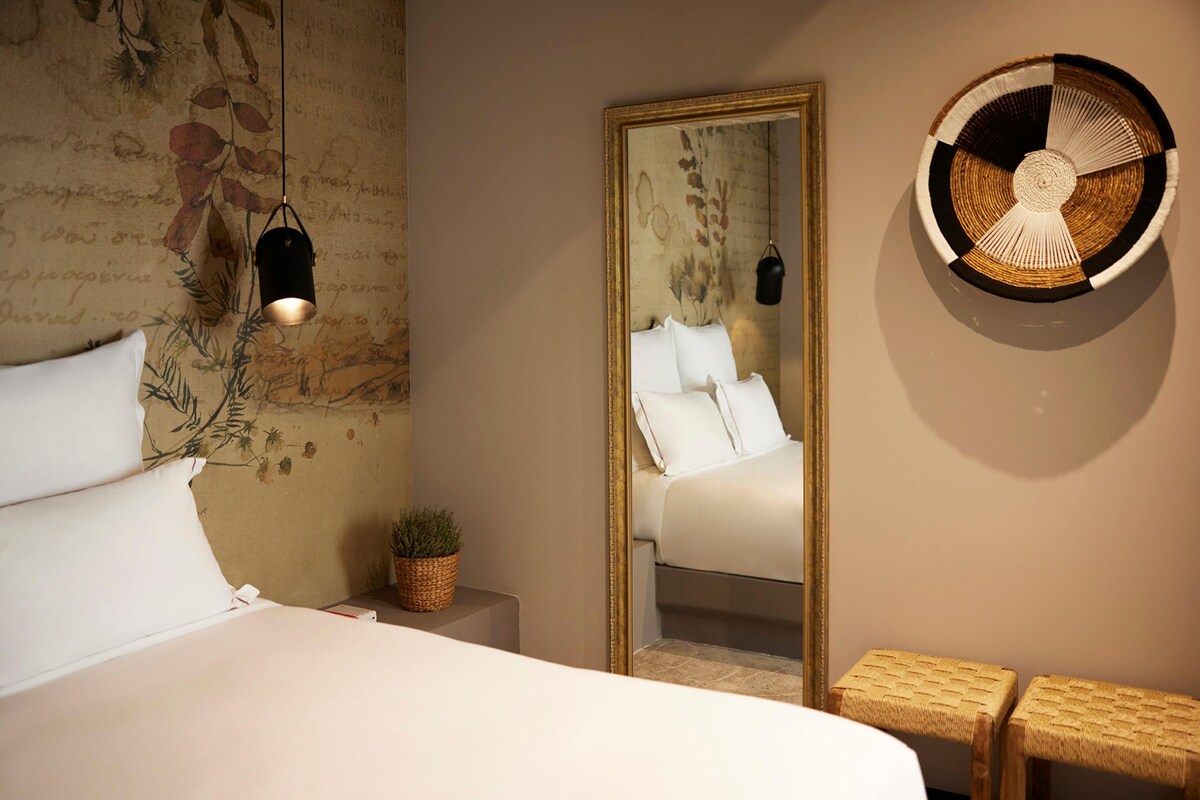A bedroom with a bed, a mirror, a hanging light fixture, and a woven wall decoration.