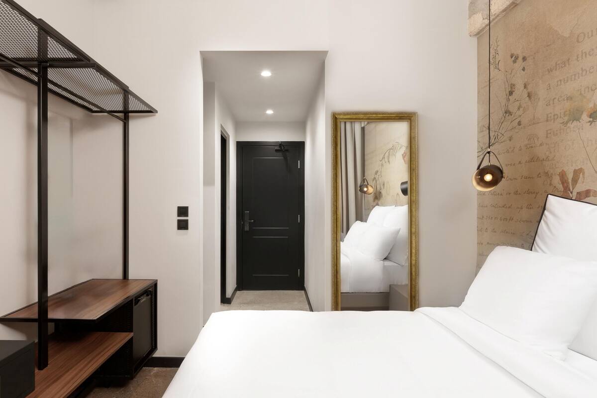 Een hotelkamer met een bed, een bureau, een spiegel en een deur naar een andere kamer.