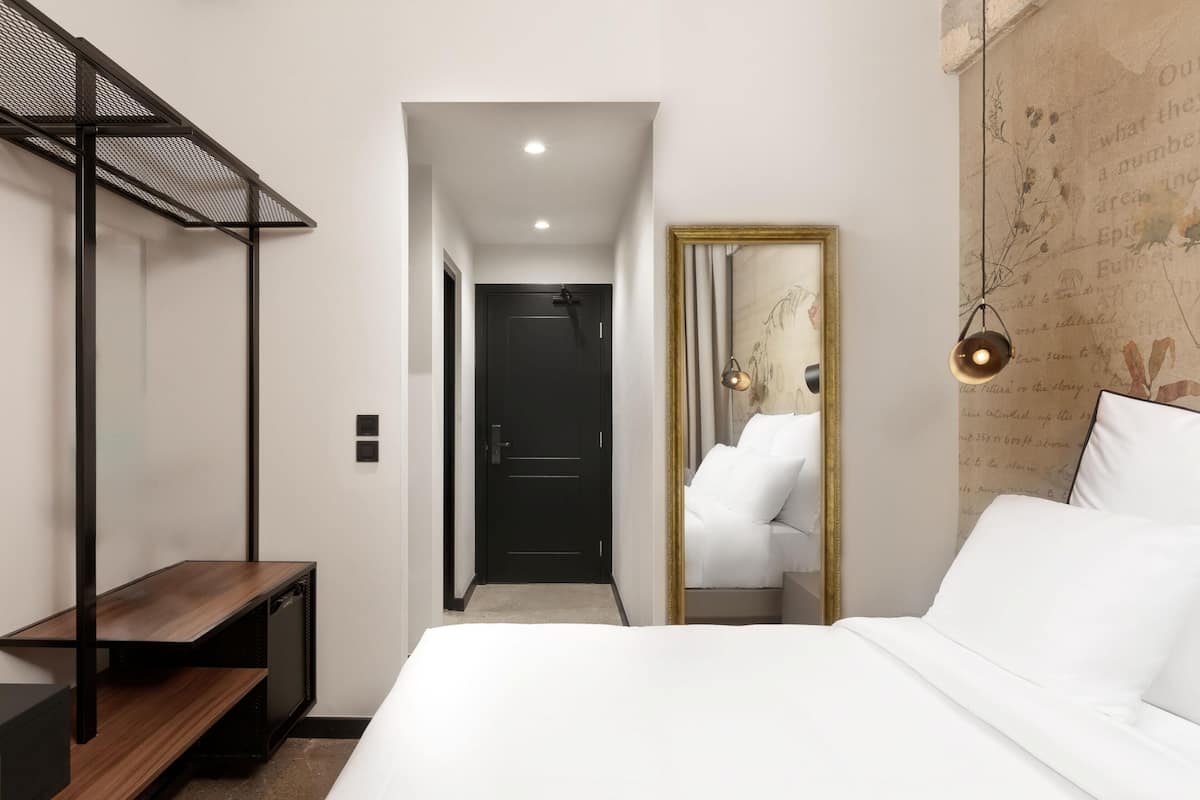 Una camera d'albergo con un letto, una scrivania, uno specchio e una porta che dà su un'altra stanza.