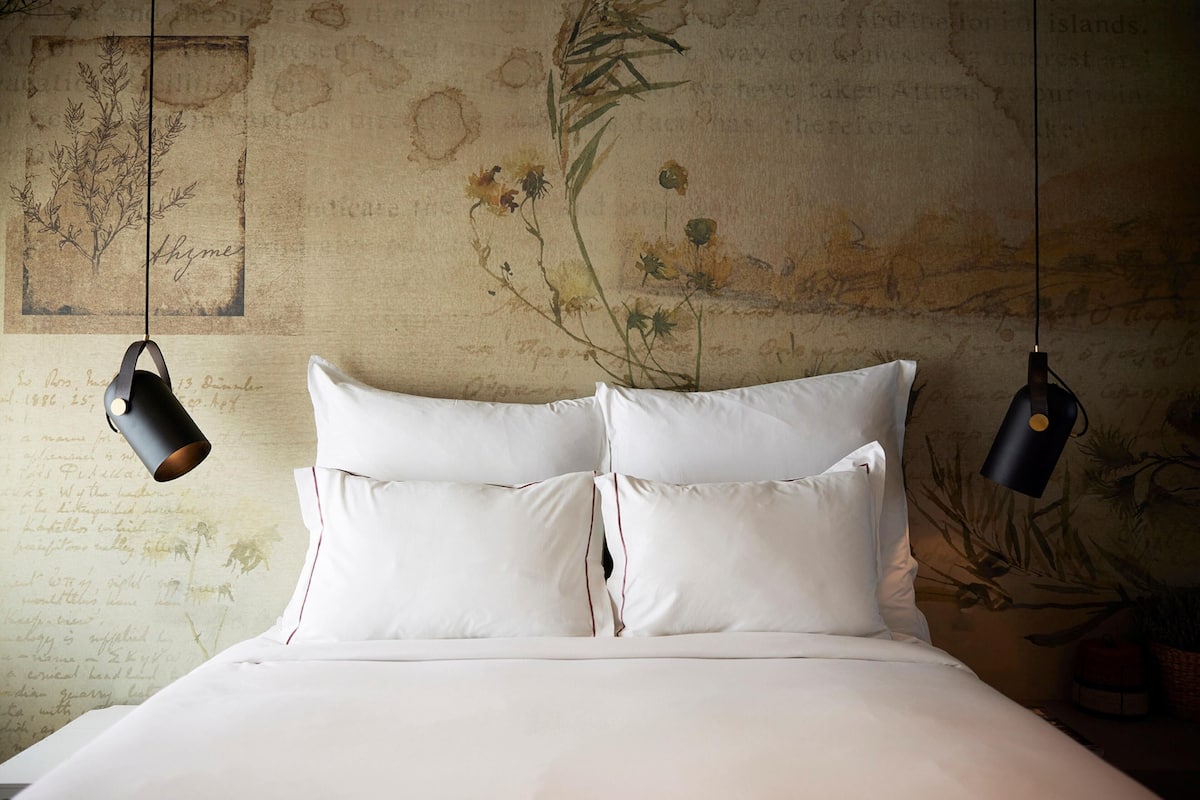 Een bed met witte lakens en twee zwarte lampen erboven.