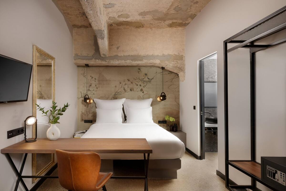 Een moderne slaapkamer met een bed, nachtkastje, stoel en bureau met een lamp.