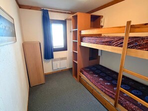 A bunk bed room with a radiator, a window with curtains, and a wooden wardrobe.