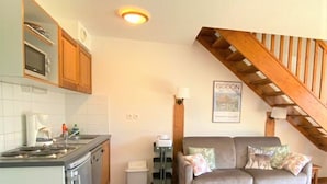 Eine kleine Küche mit Herd, Mikrowelle und Schränken, ein Sofa mit Kissen sowie eine Treppe mit Holzhandläufen.