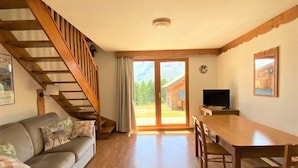 Ein gemütliches Zimmer mit einer Holztreppe, einer Couch, einem Esstisch mit Stühlen und einem Fernseher.