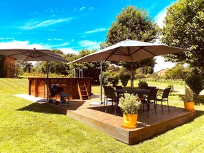 Una terraza de madera con zona de barbacoa, asientos exteriores y sombrillas.
