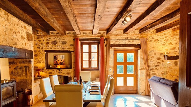 A rustic dining area with a wooden table set for four, stone walls, and a stone fireplace. - Two Historic Holiday Homes in the Dordogne — Each with a Private Heated Pool (Capdrot)