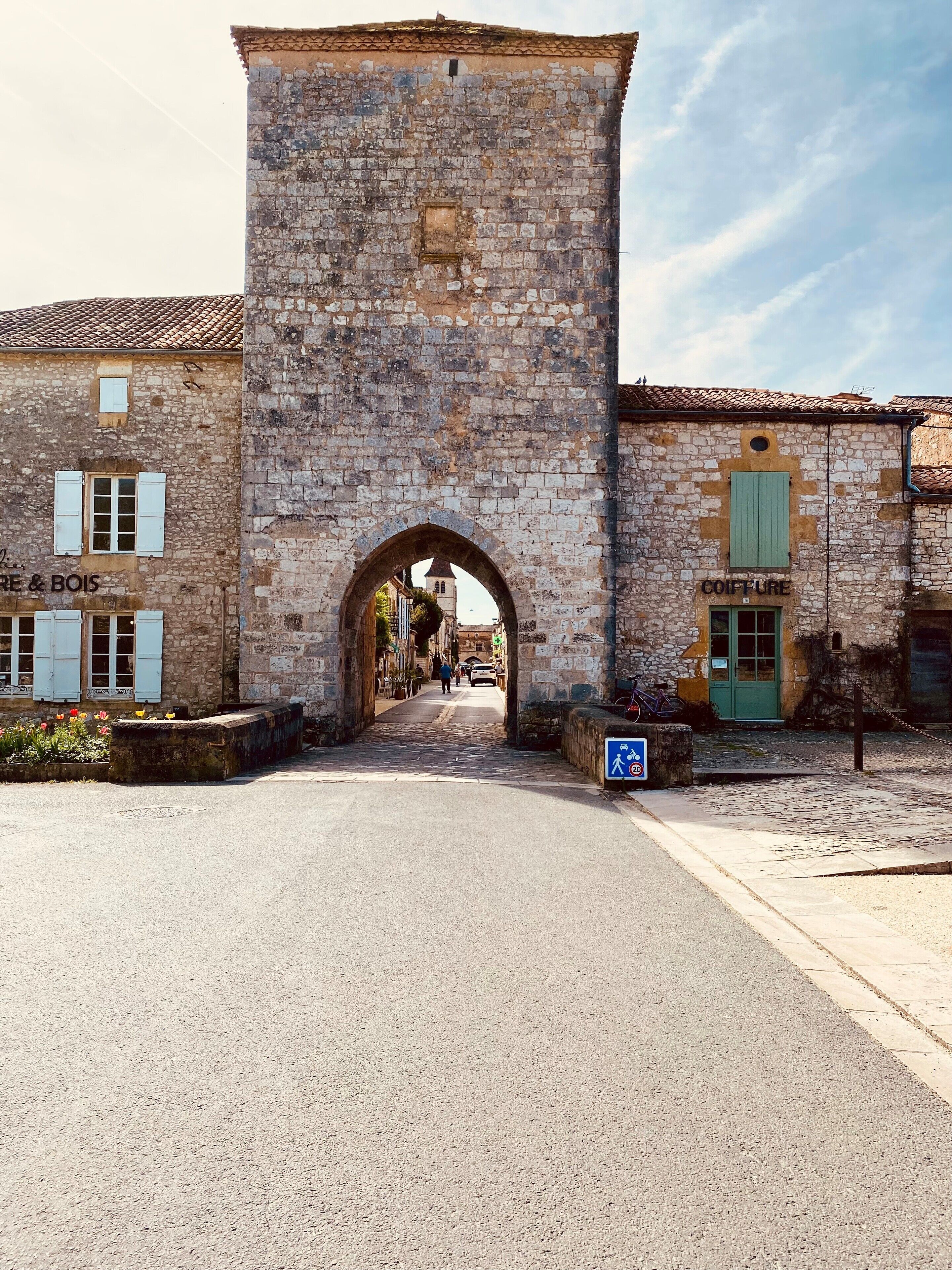 A stone archway leading to a building with a sign reading "COIFFURE".
