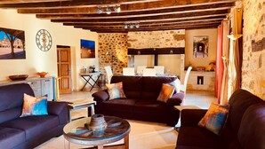 A rustic living room with dark leather sofas, a round wooden coffee table, and a stone wall. - Two Historic Holiday Homes in the Dordogne — Each with a Private Heated Pool (Capdrot)