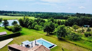 A residential property with a swimming pool, a covered patio, and a view of a green landscape with trees and a body of water. - Two Historic Holiday Homes in the Dordogne — Each with a Private Heated Pool (Capdrot)