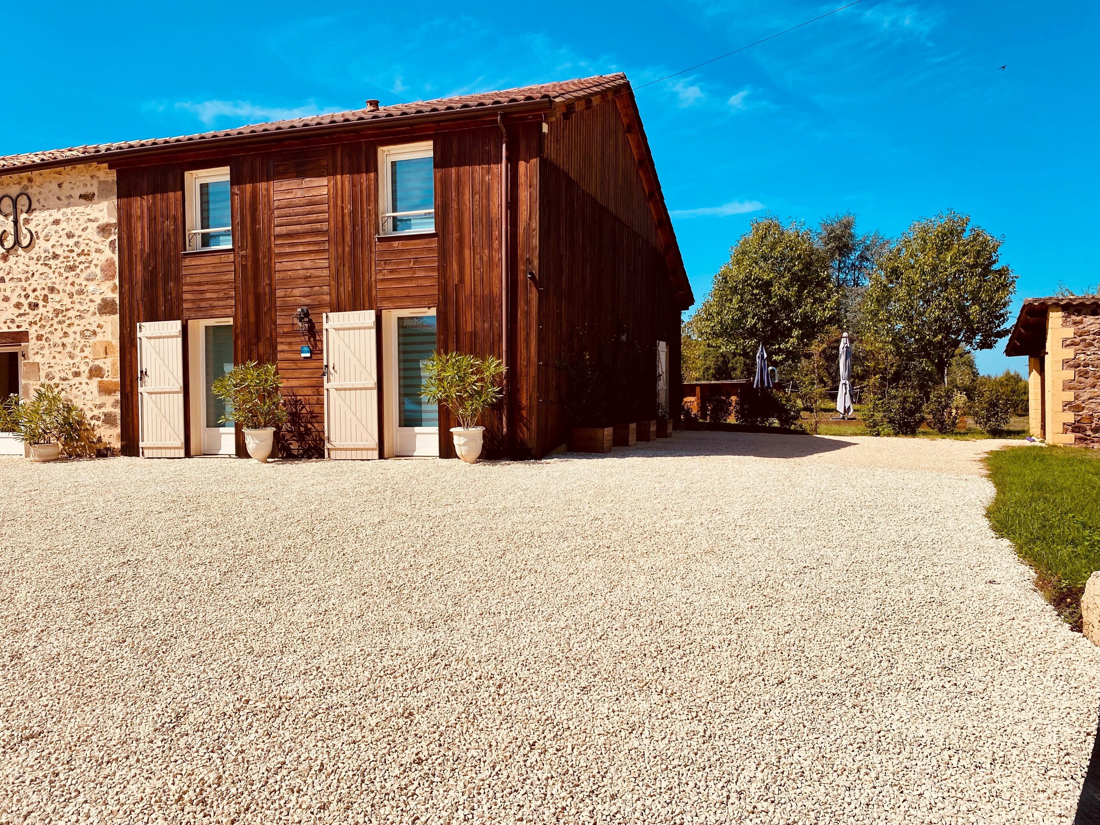 Un edificio rustico in legno con vialetto sterrato e muro in pietra.