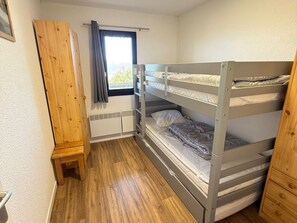 A bunk bed room with a wooden wardrobe, a window with curtains, and a radiator.