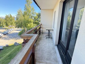 A balcony with a wooden railing, a small table, and a view of a parking lot and trees.