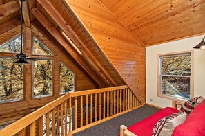 A wooden interior with a sloped ceiling, a staircase, and a window overlooking trees.