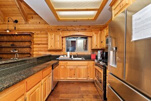 A kitchen with wooden cabinets, a granite countertop, a stainless steel refrigerator, and a skylight.