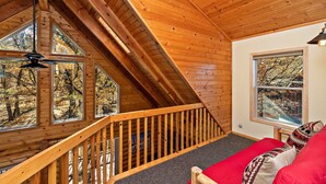 Una cabaña de madera con habitación en el altillo, ventanas amplias y una escalera.