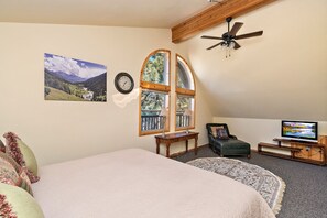 Ein Schlafzimmer mit einem großen Bett, einem Deckenventilator, einem Fernseher und einem Fenster mit Blick auf Bäume.