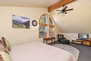 Un dormitorio con cama, televisor, reloj y ventana con vista a la montaña.