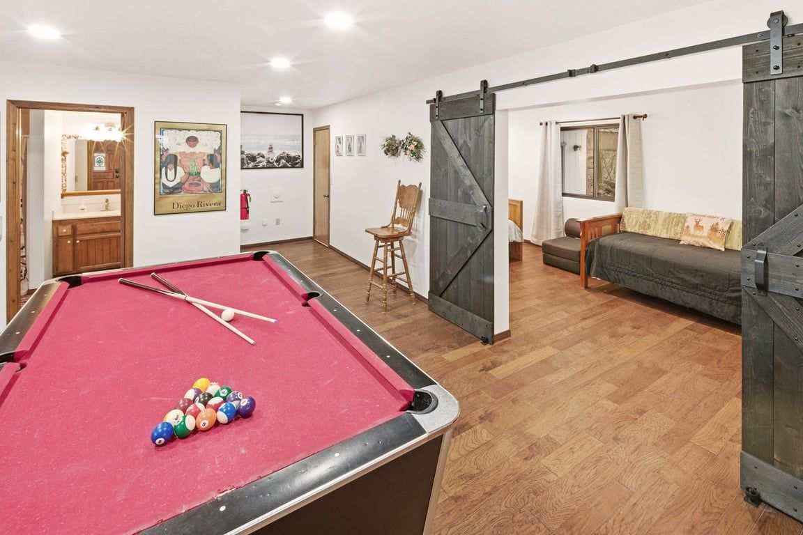 A pool table with balls, a sofa, a chair, and a sliding barn door.