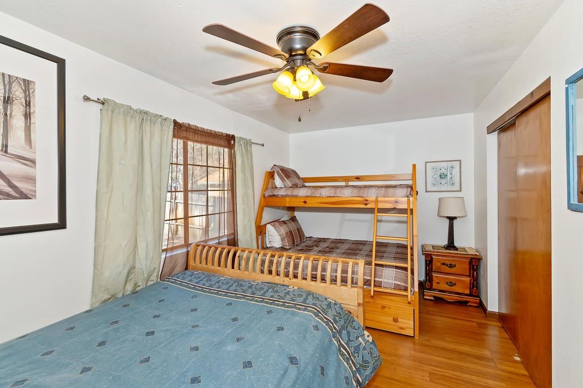 Une chambre avec un lit superposé, un ventilateur de plafond, une fenêtre avec des rideaux et une table de chevet avec une lampe.