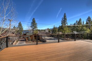 Une terrasse en bois avec une rambarde en métal, entourée d’arbres et sous un ciel dégagé.