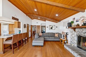 A spacious living area with a wooden ceiling, a stone fireplace, and a dining area with wooden chairs and a white table.