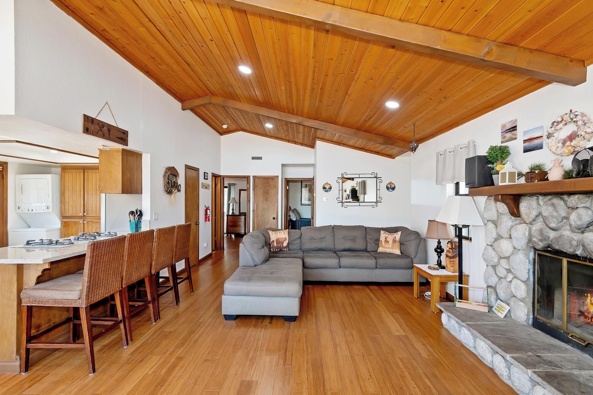 A spacious living area with a wooden ceiling, a stone fireplace, and a grey sofa.