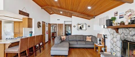 A spacious living area with a wooden ceiling, a stone fireplace, and a grey sofa.
