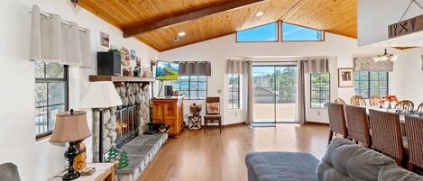 A spacious living room with a high ceiling, a fireplace, a sofa, and a dining area with chairs.