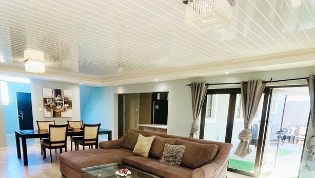A spacious living area with a large brown sofa, a glass coffee table, and a dining table with chairs. - SERENITY @  ITS HEIGHTS (Cape Town)