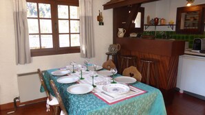 A dining area with a table set for six, a window with curtains, and a kitchen area with shelves and a sink. - Unique chalet for 8 ppl, pets welcome, parking (Les Contamines-Montjoie)