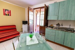 A compact living space with a kitchenette, a dining area with a glass table, a sofa, and a TV. - One Bedroom Apartment with Garden (Guardistallo)